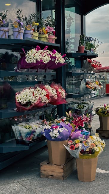 A display of fresh floral arrangements and bouquets at a flower shop, featuring a variety of colorful flowers including pink, white, and purple blooms. The arrangements are wrapped in pastel-colored, 